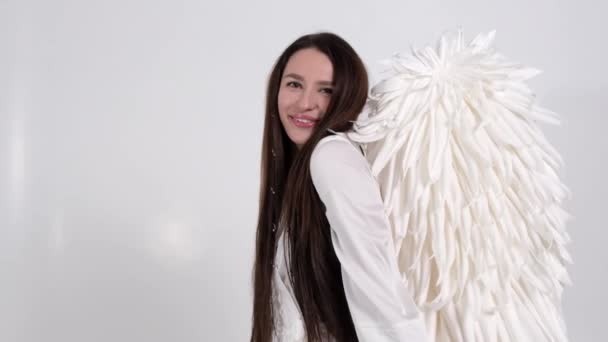 Portret van een lachende vrouw naar het beeld van een engel toont ze handen een hart. Meisje met lang recht haar op een witte achtergrond. Valentijnsdag concept. Langzame beweging - Video
