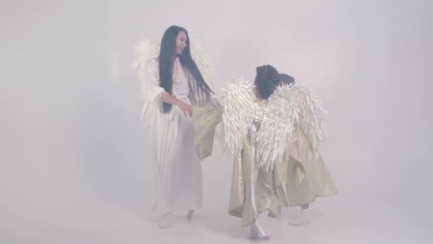 Un encantador video de una madre con niños en humo en forma de ángeles con alas blancas, tomados de la mano y dando vueltas en el estudio en blanco. Vídeo 4k - Metraje, vídeo