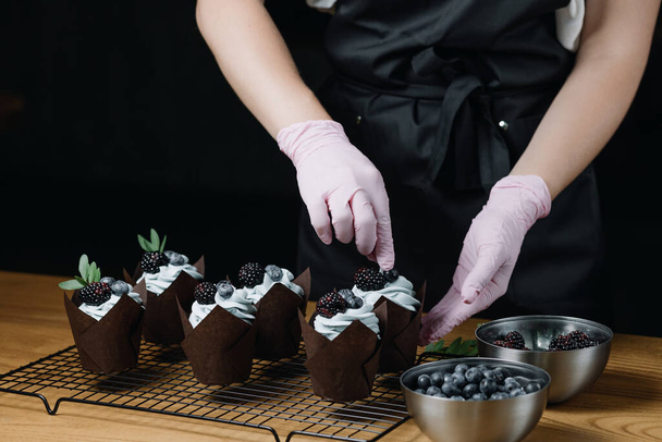  Csokis muffinok krémkeverékkel. A női kezek friss bogyókkal töltik meg a muffinokat. Kiváló minőségű fénykép - Fotó, kép