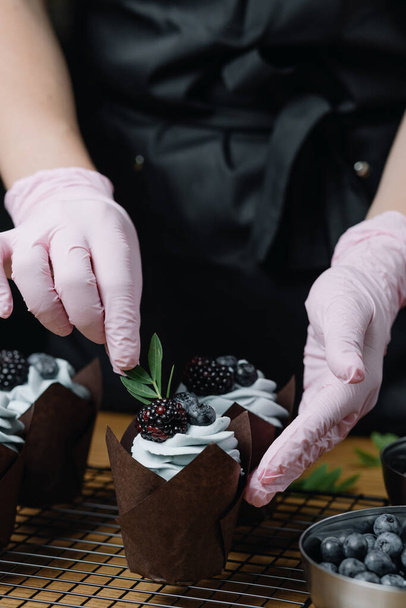  Шоколадные кексы со сливками. Женские руки украшают кексы свежими ягодами и декоративными травами. Высокое качество фото - Фото, изображение