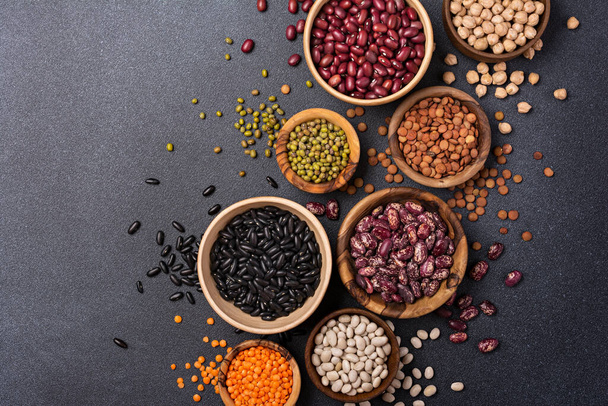 Top view of different beans, lentils, mung or maash, chickpeas in bowls on dark concrete background - Фото, изображение