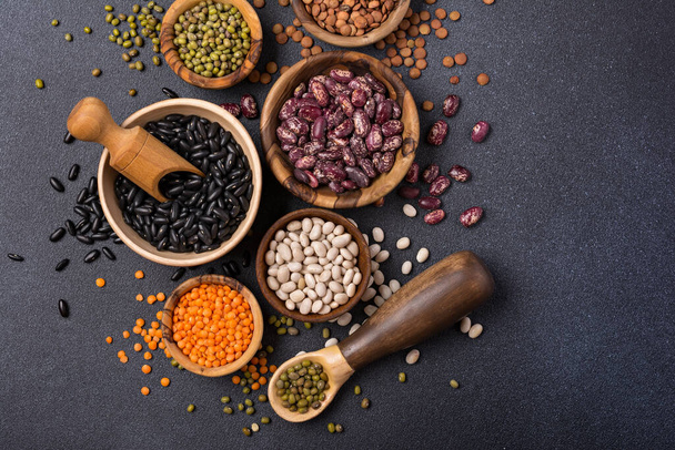 Top view of different beans, lentils, mung or maash in bowls on dark concrete background - Foto, imagen