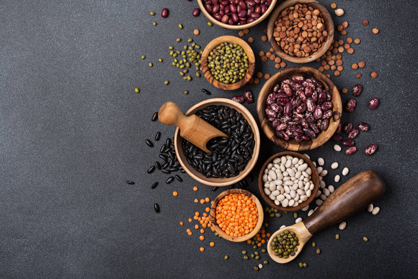 Top view of different beans, lentils, mung or maash in bowls on dark concrete background - Fotó, kép
