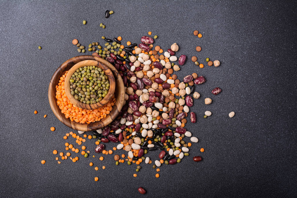 Top view of different beans, lentils, mung or maash, chickpeas in wooden bowls on dark concrete background - Foto, immagini