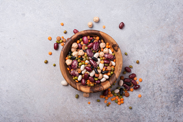 Top view of different beans, lentils, mung, chickpeas in wooden bowl on grey concrete background - Foto, Imagem