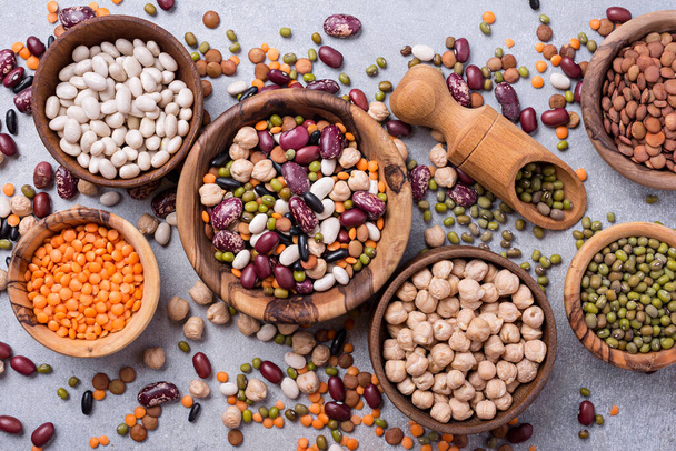 Top view of different beans, lentils, mung, chickpeas in wooden bowls for tasty meals on grey concrete background - Fotó, kép