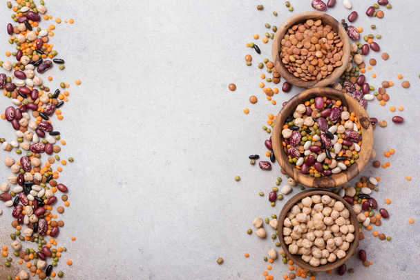 Top view of different beans, lentils, mung, chickpeas in wooden bowls for tasty meals on grey concrete background with copy space - Foto, Imagem