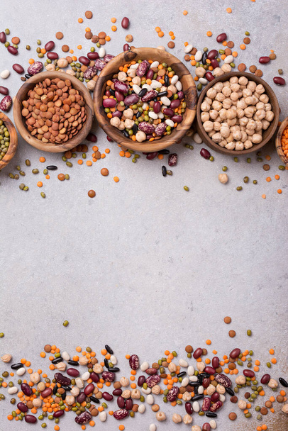 Top view of different beans, lentils, mung, chickpeas in wooden bowls for tasty meals on grey concrete background with copy space - 写真・画像