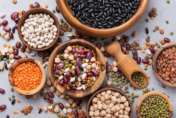 Top view of different beans, lentils, mung, chickpeas in wooden bowls for tasty meals on grey concrete background - Foto, immagini