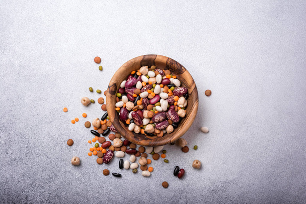 Top view of different beans, lentils, mung, chickpeas in wooden bowl on grey concrete background - Фото, изображение