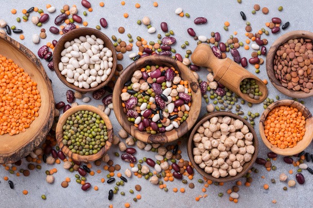 Top view of different beans, lentils, mung, chickpeas in wooden bowls for tasty meals on grey concrete background - Photo, image