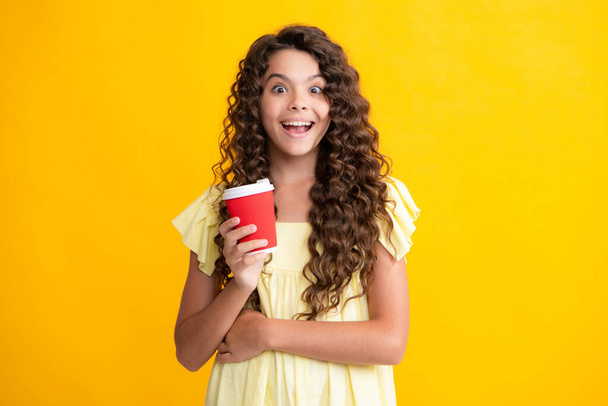 Child with coffee or tea cup isolated on yellow studio background. Teenage girl with take away beverage. Excited teenager, glad amazed and overjoyed emotions - Foto, Imagen