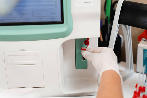 研究室のクローズアップで分析器の血液分析.研究室のアシスタントは血液学的分析を行います.研究室の医療機器。血液の生化学的および血液学的解析 - 写真・画像