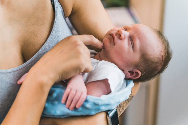 Adorable infant baby boy with cute hair, wrapped in a blanket, sleeping peacefully at home, young caucasian mom holding her son in her arms and touching his chin. High quality photo - Photo, Image
