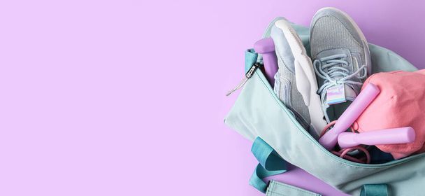 Bolsa con ropa deportiva y equipo sobre fondo lila con espacio para texto - Foto, Imagen