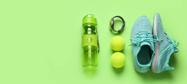 Zapatos deportivos, botella de agua, rastreador de fitness y pelotas de tenis sobre fondo verde - Foto, imagen