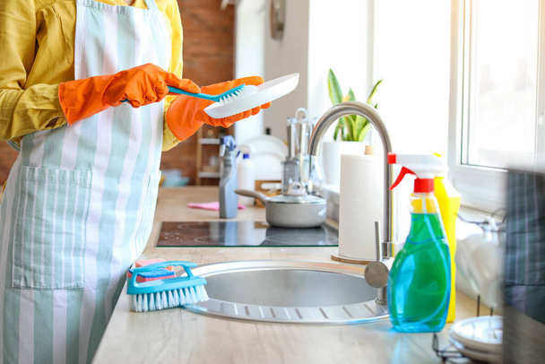Young woman cleaning plate with brush in kitchen - Foto, Bild
