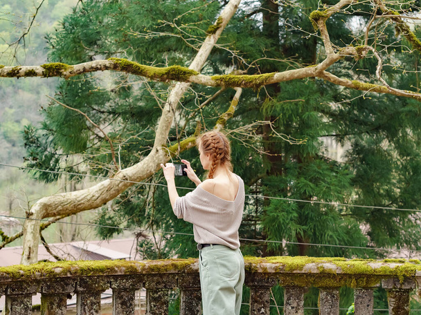 Una mujer toma una foto en el teléfono de un parque abandonado musgoso - Foto, imagen