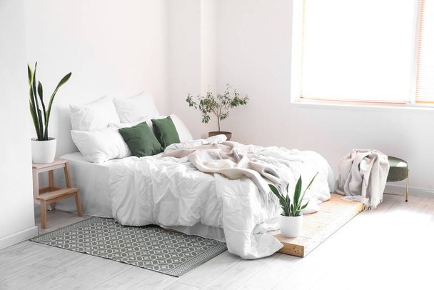 Интерьер светлой комнаты с большой кроватью и комнатными растениями - Фото, изображение