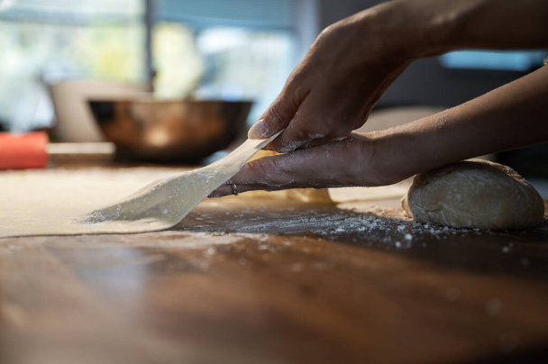Low angle view of a woman stretching and pulling homemade vegan pastry dough on a domestic flour dusted dining table. - Φωτογραφία, εικόνα