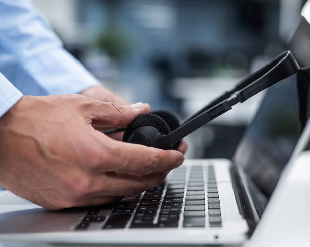 A man puts a headset on a laptop keyboard in the office - Φωτογραφία, εικόνα