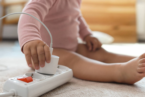 Cute baby playing with charger and power strip on floor at home, closeup. Dangerous situation - Foto, Imagem