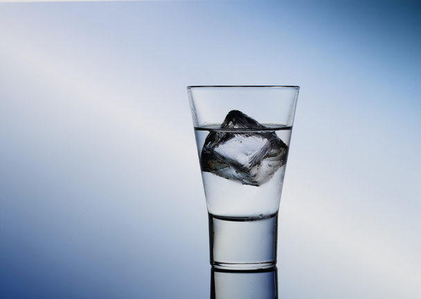Short drink glass with clear liquid and ice cubes - Фото, изображение