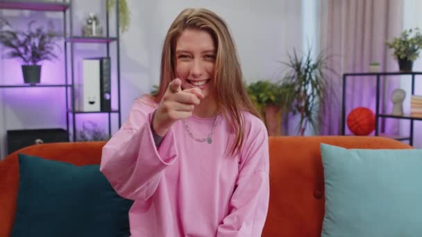 Hey you. Portrait of adult girl smiling excitedly and pointing to camera, choosing lucky winner, indicating to awesome you, inviting, approve. Young woman at modern home apartment living room on couch - Záběry, video