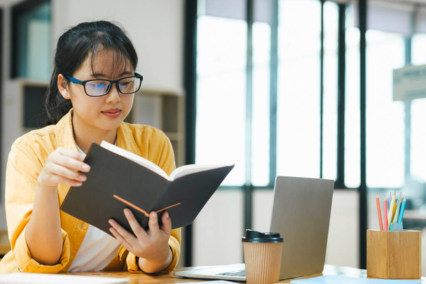Glückliche junge asiatische Frau langweilt sich, viele Bücher zu lesen. Student studiert harte Prüfung in einem Heim. - Foto, Bild