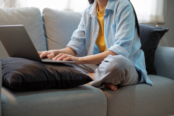 Close up of women working and studying using laptop at home. Women working, studying, researching using laptop while sitting on couch at home. Close up. Education and online learning concept. - 写真・画像