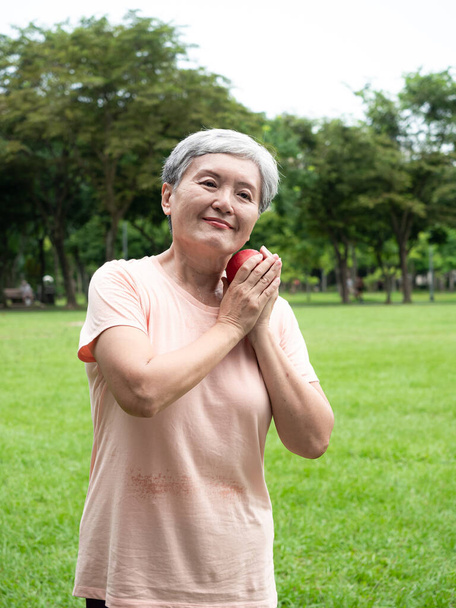 Портрет щасливої старшої дорослої літньої жінки Азії, яка посміхається стоячи з мірною стрічкою і тримаючи в парку яблуко
. - Фото, зображення