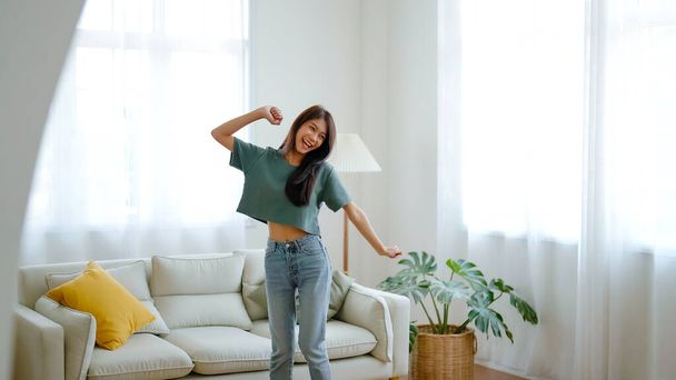 Genç Asyalı kadın evdeki oturma odasında yerde dans ediyor. Mutlu Asyalı kadın gülümsemesi evde dinleniyor, sağlıklı zihinsel sağlık ve refah. - Fotoğraf, Görsel