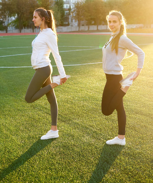 Duas lindas meninas de esportes se exercitando juntas em um gramado no início da manhã
. - Foto, Imagem