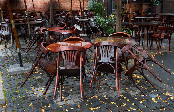 Деревянные стулья, опирающиеся на столики в закрытом кафе или ресторане утром после дождя - Фото, изображение