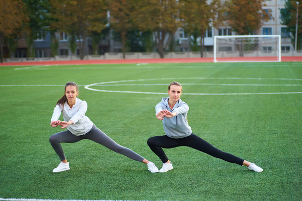 Two beautiful sports girls exercising together on a lawn in the early morning. - Fotó, kép