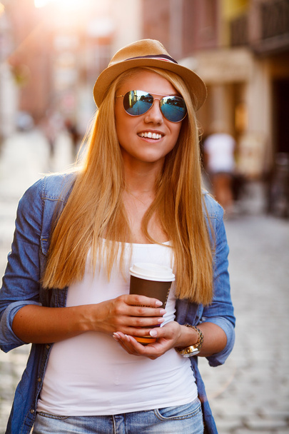 若いスタイリッシュな女性は街の通りに行くためにコーヒーを飲む - 写真・画像