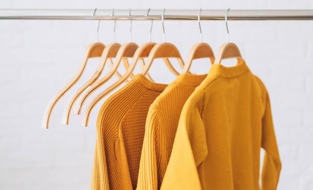Sweats-shirts jaunes sur cintres en bois accrochés sur un rale de barre de fer. - Photo, image