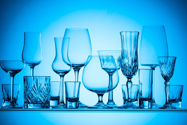 Silhouetten van verschillende lege glazen op een blauwe achtergrond. - Foto, afbeelding