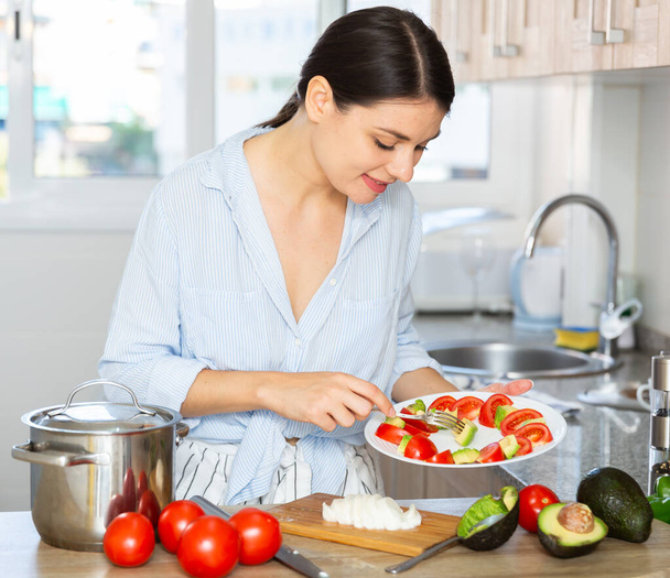 Housewife prepares tomato and avocado salad in the kitchen - Foto, Imagen