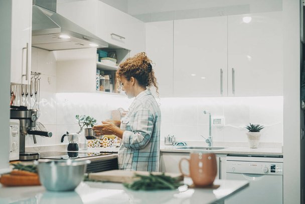 Nainen kokkaamassa kotona keittiössä yksin. Todellinen yksi elämäntapa itsenäisille naispuolisille ihmisille. Kotiäiti valmistaa lounasta perheelle. Näkymä nainen käyttää potin ja valmistaa ruokaa sisätiloissa. - Valokuva, kuva