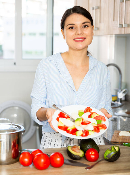 Housewife prepares tomato and avocado salad in the kitchen - Фото, зображення