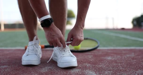 Een man die veters bindt aan witte tennisschoenen op de tennisbaan. Sportschoenen van hoge kwaliteit voor tennis - Video