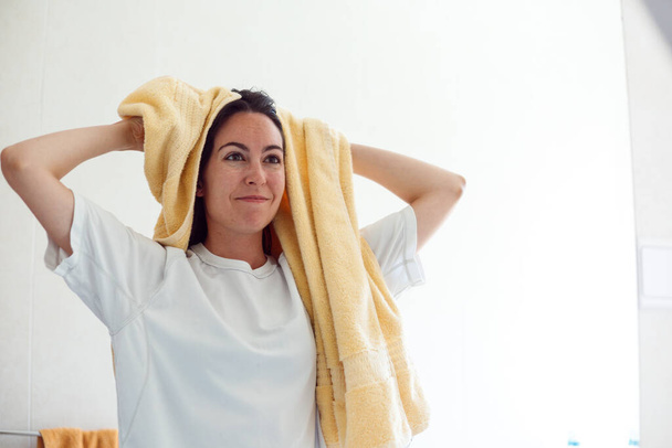Vera giovane donna asciugatura capelli bagnati con asciugamano, essendo contento dopo aver fatto il bagno, posa su sfondo bianco, ha espressione allegra - Foto, immagini