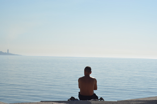 Hombre mirando el mar sentado en una gran roca
 - Foto, imagen