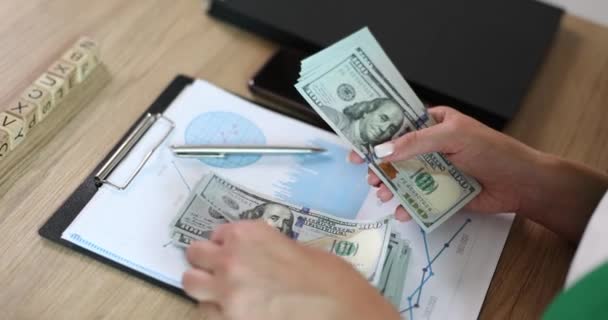 Mão feminina contando dinheiro no escritório em gráficos financeiros. Muitas centenas de dólares e contar no local de trabalho close-up. - Filmagem, Vídeo