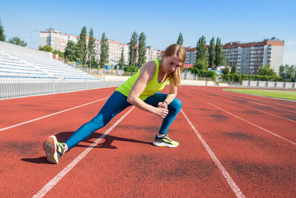 Het meisje warmt op in het stadion. Sportvrouw strekt beenspieren uit voor het joggen. Training in het Stadssportstadion. - Foto, afbeelding