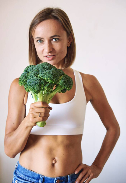 young woman dressed in white t-shirt showing with broccoli. High quality photo - Zdjęcie, obraz