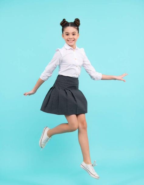 Funny excited jumping teenager. Happy schoolgirl, positive and smiling emotions of teen girl. Full length jump of teenager girl on blue isolated studio wear casual skirt and shirt - Foto, Imagen