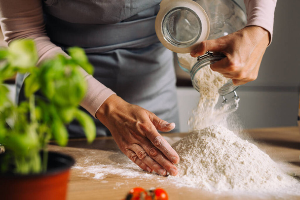 woman prepares dough in home kitchen, holding flour - Zdjęcie, obraz