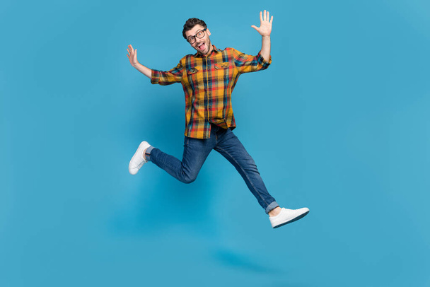 Full length portrait of carefree energetic man jumping enjoy free time isolated on blue color background. - 写真・画像